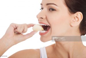 closeup-of-young-woman-eating-garlic-against-white-background-picture-id947392324
