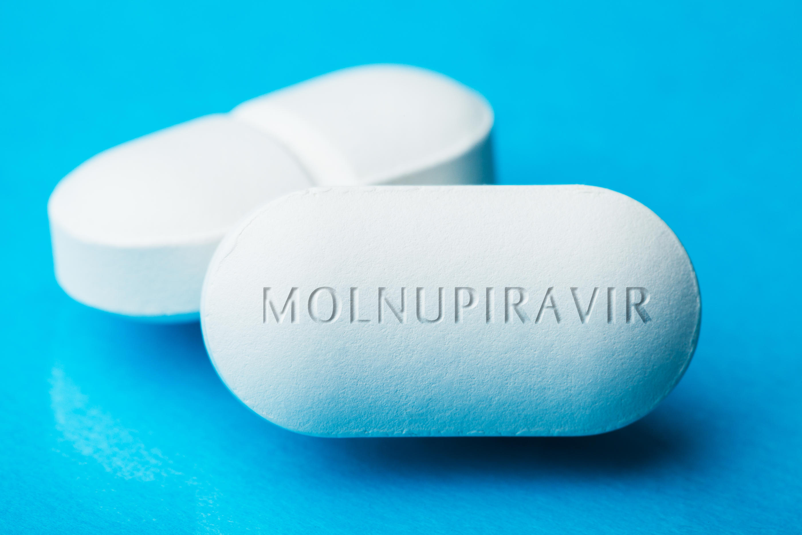 COVID-19 experimental antiviral drug MOLNUPIRAVIR, two white pills with letters engraved on side, potential experimental WHO Coronavirus cure, pandemic outbreak crisis, isolated on blue background
