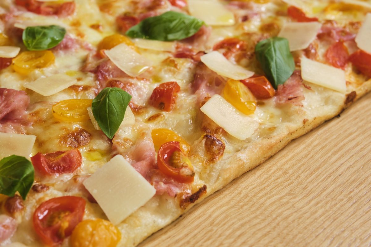 La pizza dell’estate 2023 all’insegna della tradizione romana con prosciutto cotto, pomodori ciliegini e datterini gialli, basilico e petali di Parmigiano Reggiano