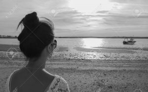 Black and white photo of young asian woman standing at the beach and looking out to the sea. concept lonely girl, Feeling sad
