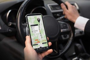 Un uomo in auto con in mano uno smartphone. Sta usando l'applicazione Finder Portal di PAJ per controllare gli allarmi del suo localizzatore GPS.