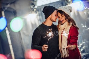 Young romantic couple is having fun outdoors in winter before Christmas with Bengal lights. Enjoying spending time together in New Year Eve. Two lovers are hugging and kissing in Saint Valentine's Day